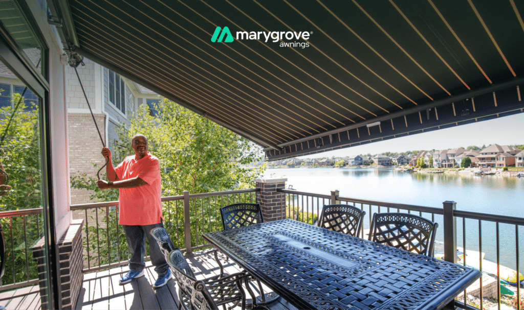 Man adjusting the pitch of a Marygrove retractable awning over a lakeside patio.