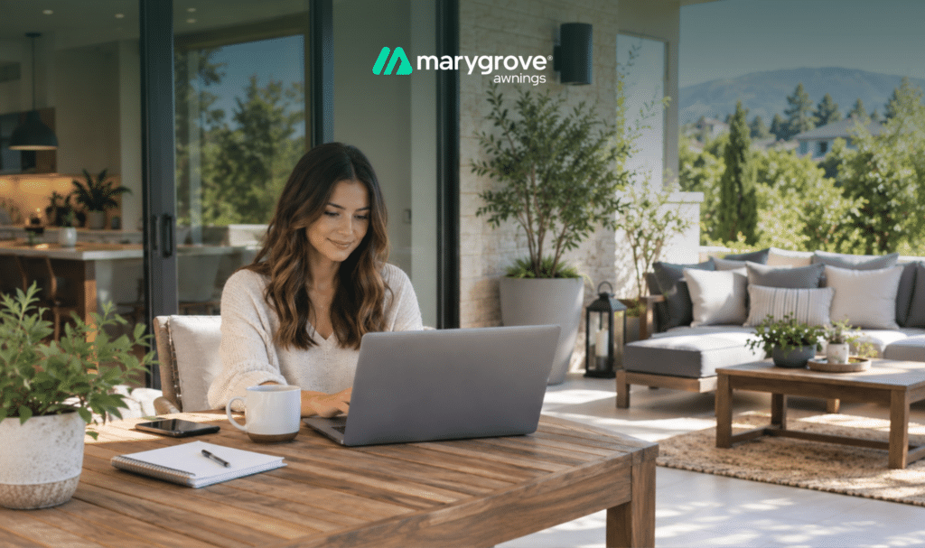 Smiling woman using a laptop at a wooden table on a covered patio with lounge seating, with a Marygrove logo