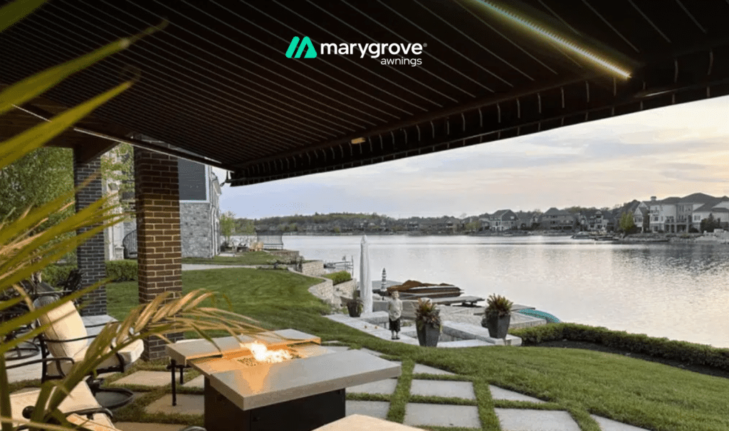 Outdoor patio with a retractable awning, fire pit, and seating area overlooking a lake.