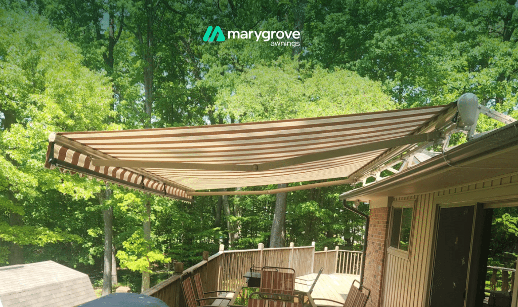 Brown and cream striped Marygrove retractable awning extended over a backyard deck surrounded by trees.